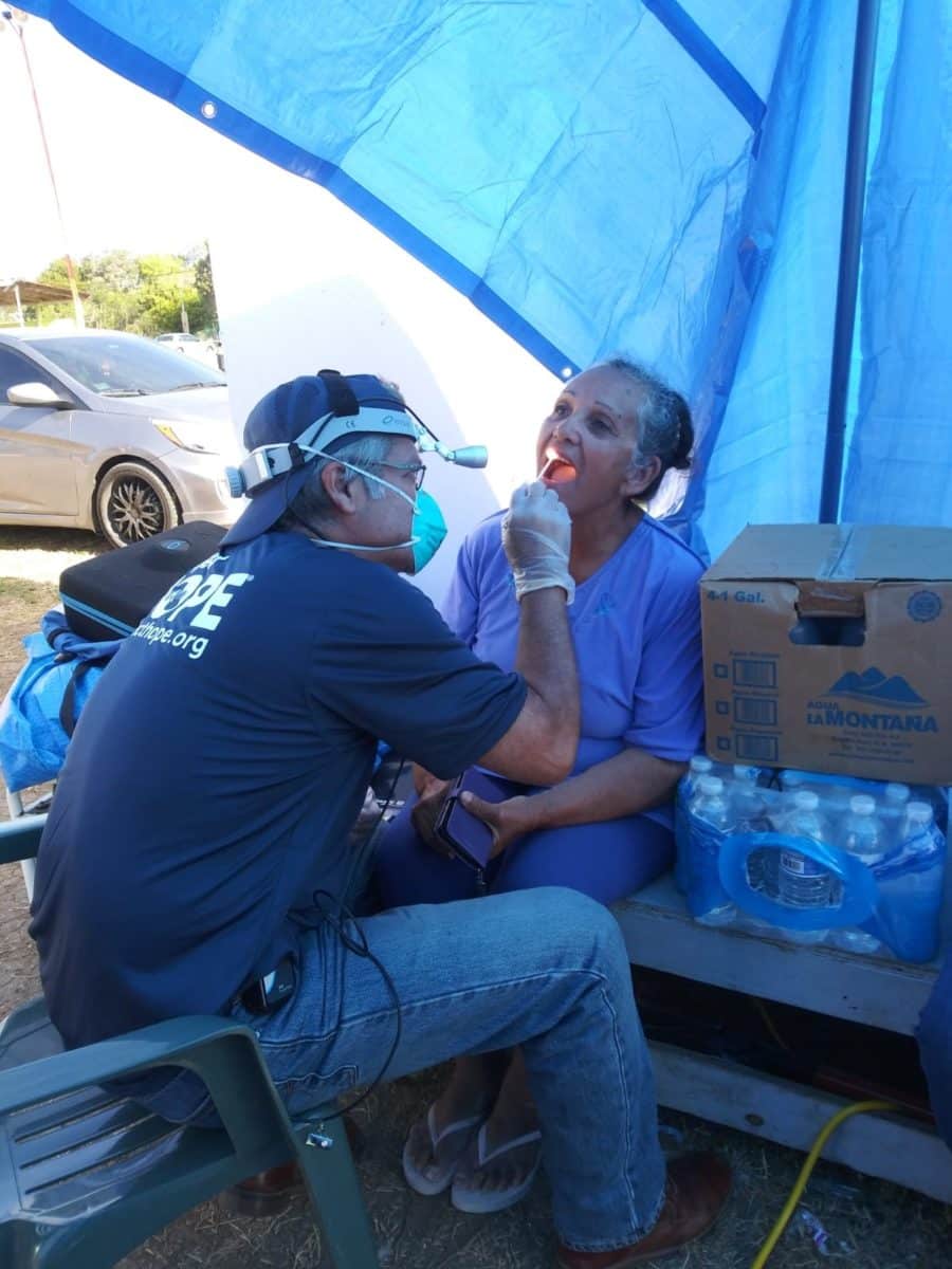 A dentist wearing an Enova Illumination headlight examines the mouth of a patient on a mission trip.